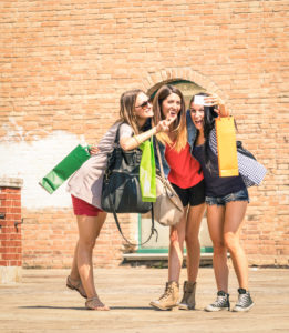 Group of happy best friends with shopping bags taking selfie